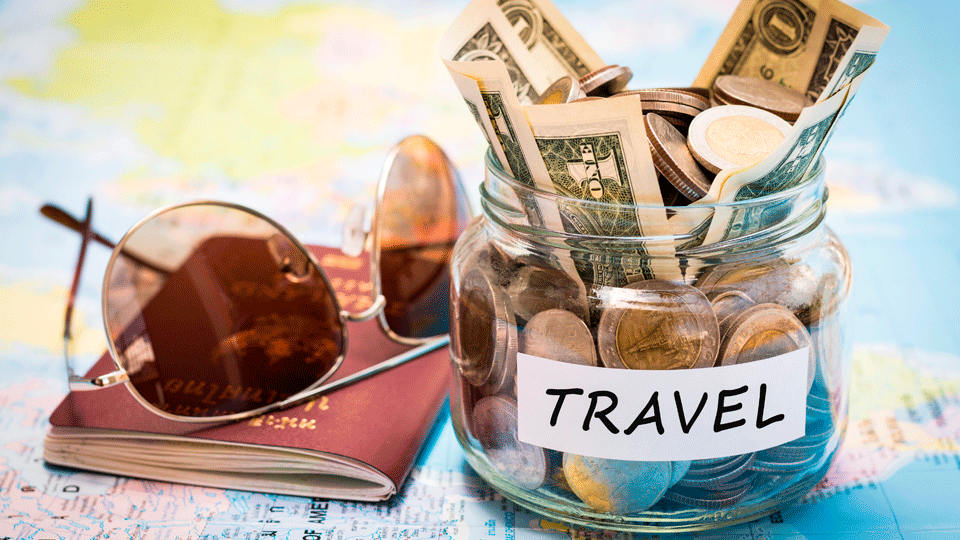 Un frasco de cristal con billetes y monedas, al lado de unas gafas de sol y un pasaporte. Un frasco de cristal con billetes y monedas, al lado de unas gafas de sol y un pasaporte.
